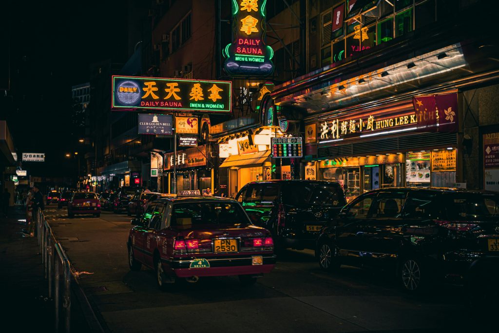 Explore the bustling nightlife of Hong Kong with vibrant neon signs and iconic taxis on a lively street.