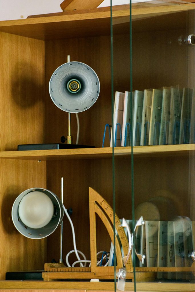 Close-up of a wooden shelf with lamps, books, and office equipment behind glass.