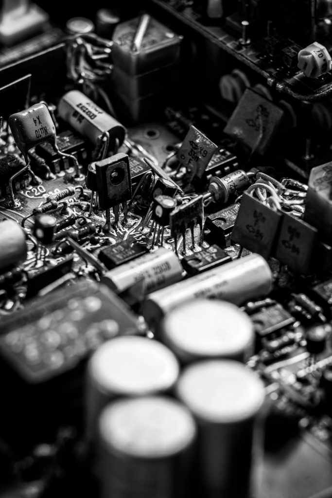 Detailed black and white close-up of an electronics circuit board with capacitors and transistors.