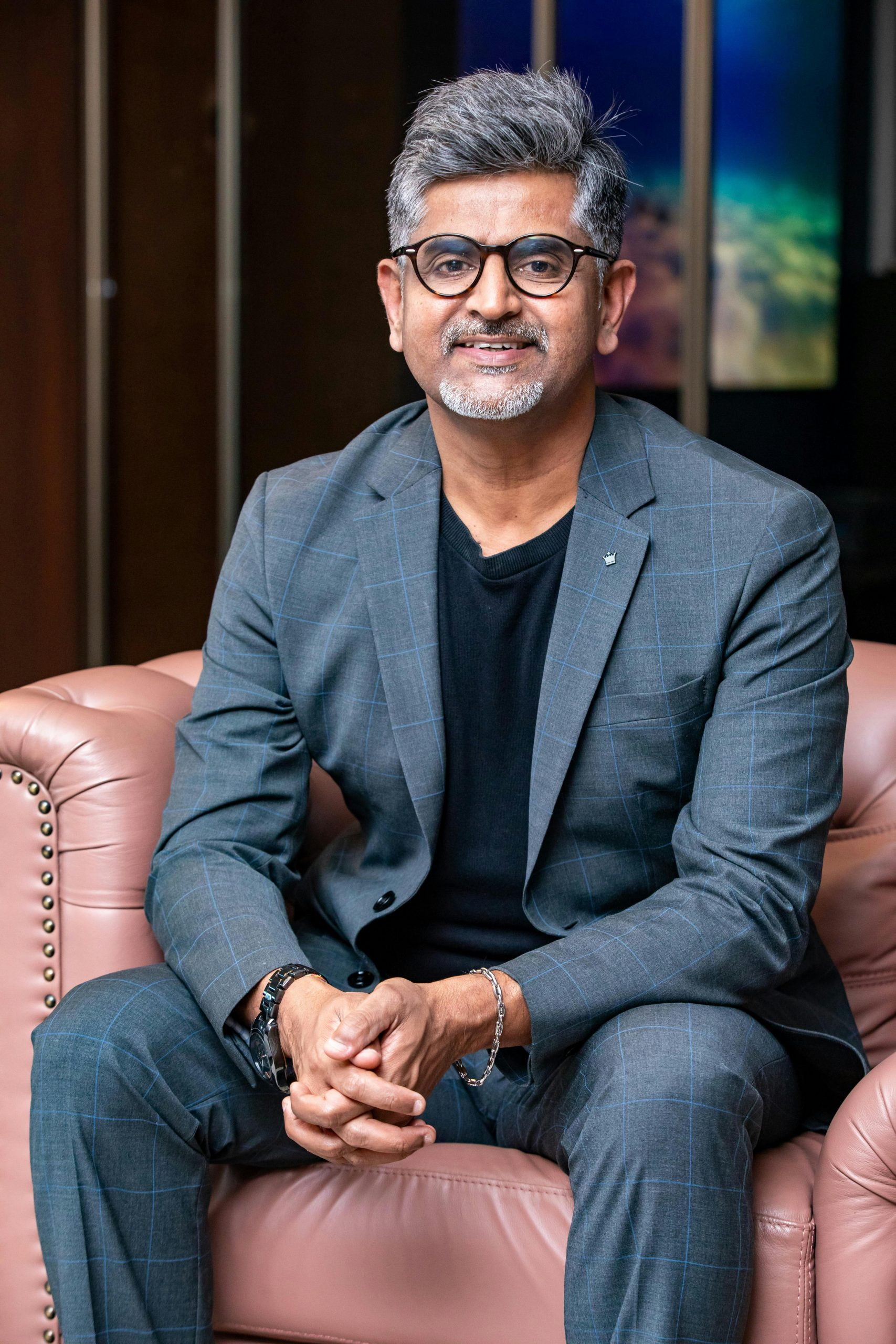A man in a stylish business suit sits confidently on a leather couch indoors.